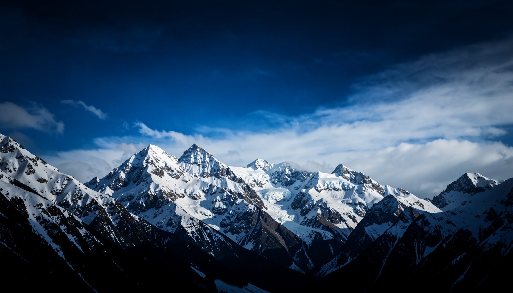Montañas nevadas bajo un cielo azul intenso con nubes ligeras, tonos blancos, azules y grises, pureza y grandeza.